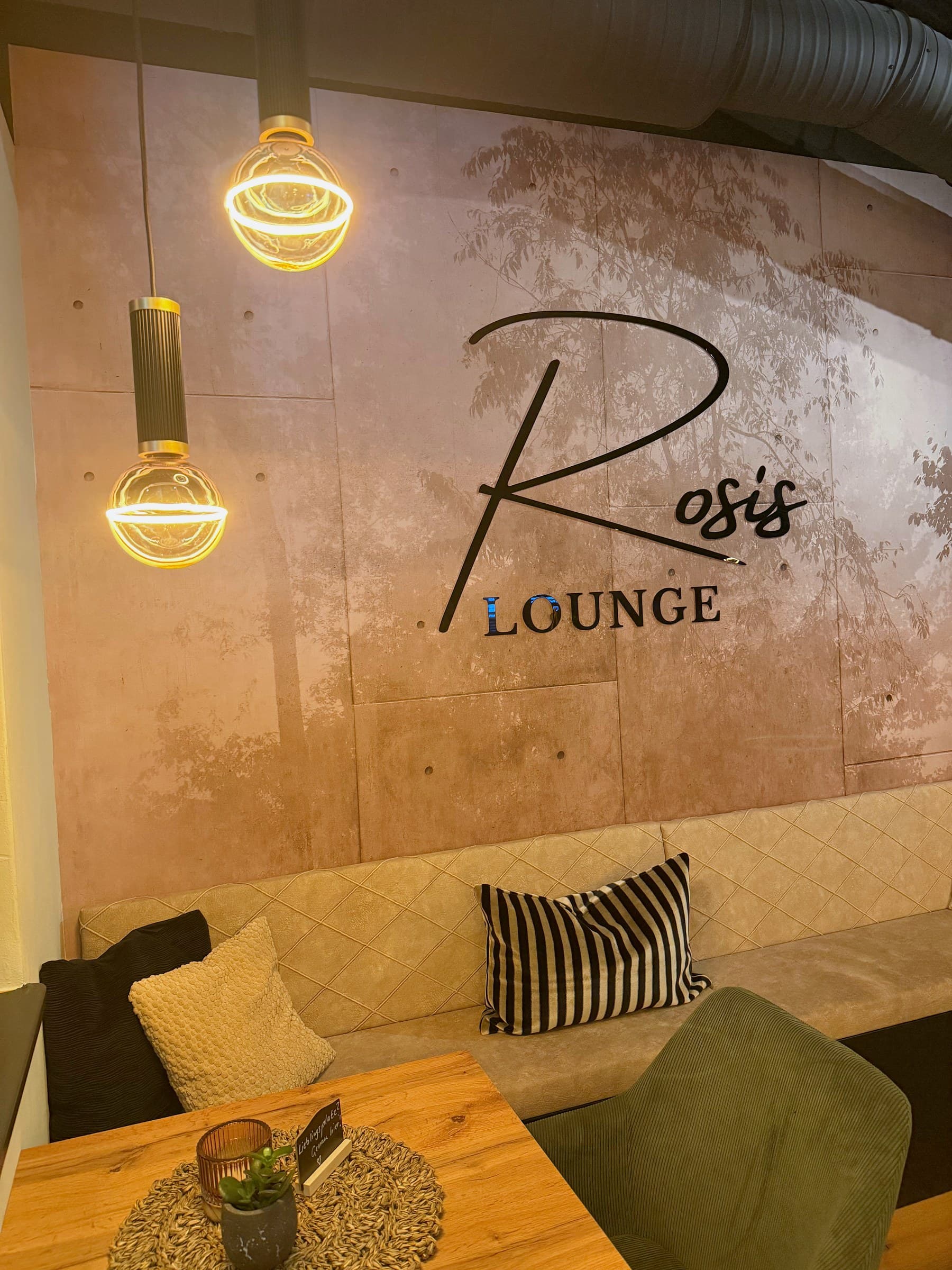 Sitzecke unter dem Schriftzug Rosi's Lounge mit Pendelleuchten