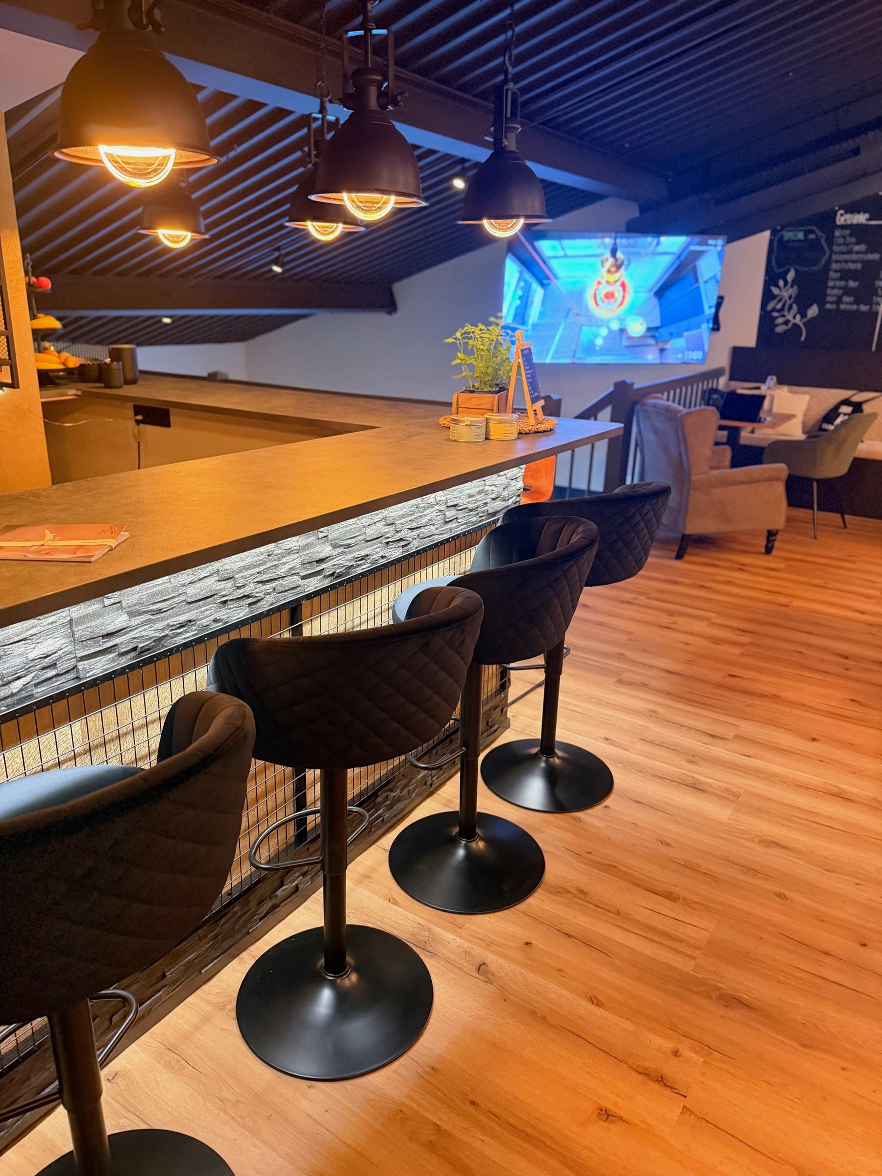 Bar mit dunklen Hockern, Steinverkleidung und Bildschirm im Hintergrund