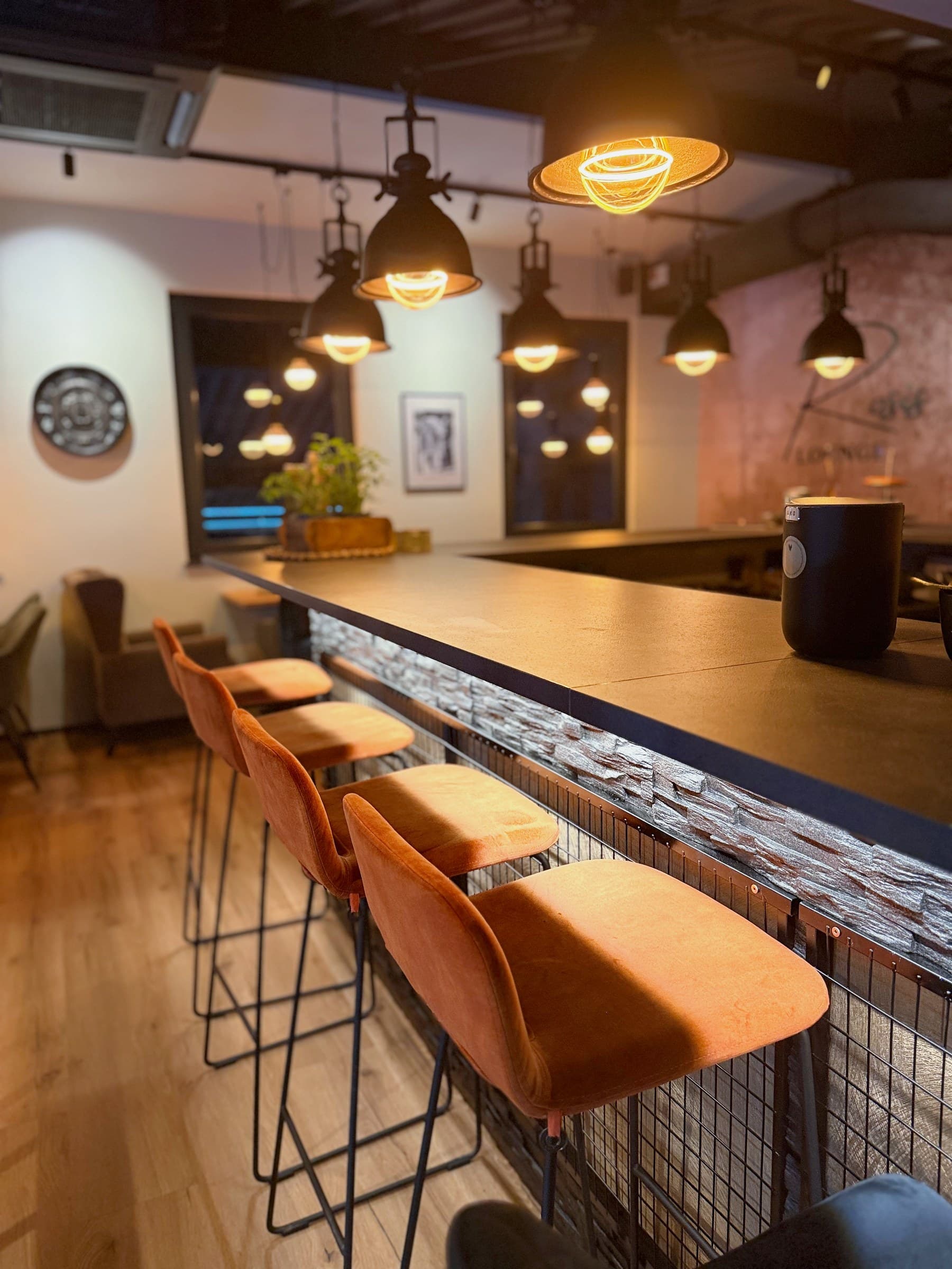 Theke mit orangefarbenen Hockern und warmen Hängeleuchten